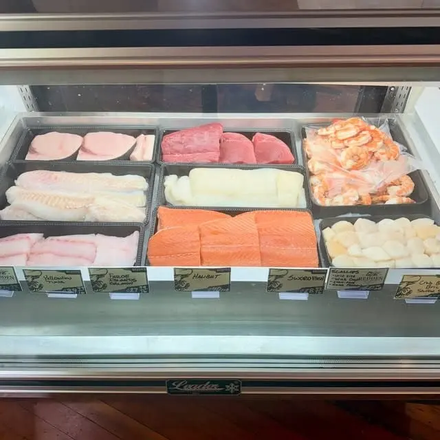 The seafood case with trays of salmon, white fish fillets, tuna, shrimp and scallops behind the glass