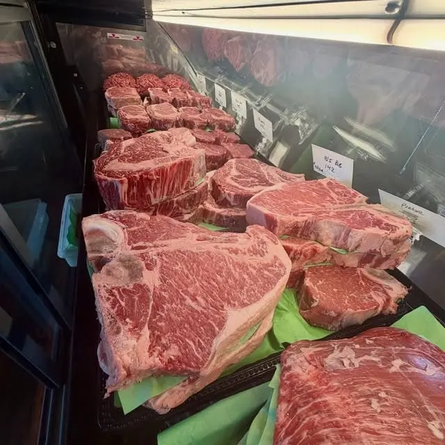 The butcher case filled with thick, marbled bone-in and boneless steaks on green paper
