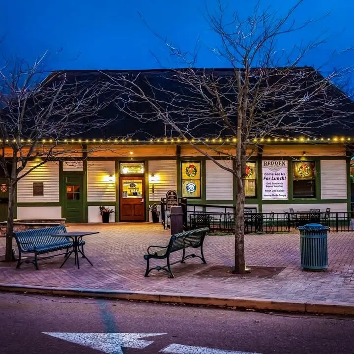 The Madeira depot at dusk, with string lights along the eaves, wreaths in the windows and benches on the brick plaza out front