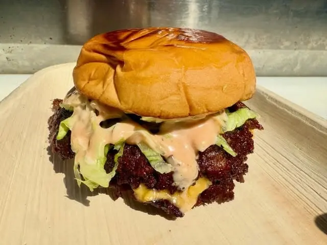 A smash burger with two crispy patties, melted cheese, lettuce and sauce on a toasted bun